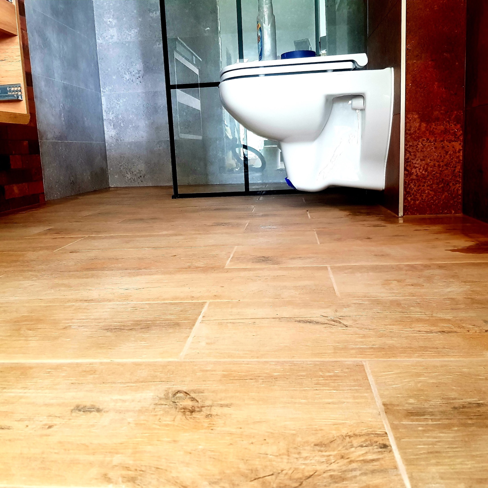 Nowoczesna łazienka z drewnopodobną podłogą, wiszącą toaletą i kabiną prysznicową z czarnymi profilami.