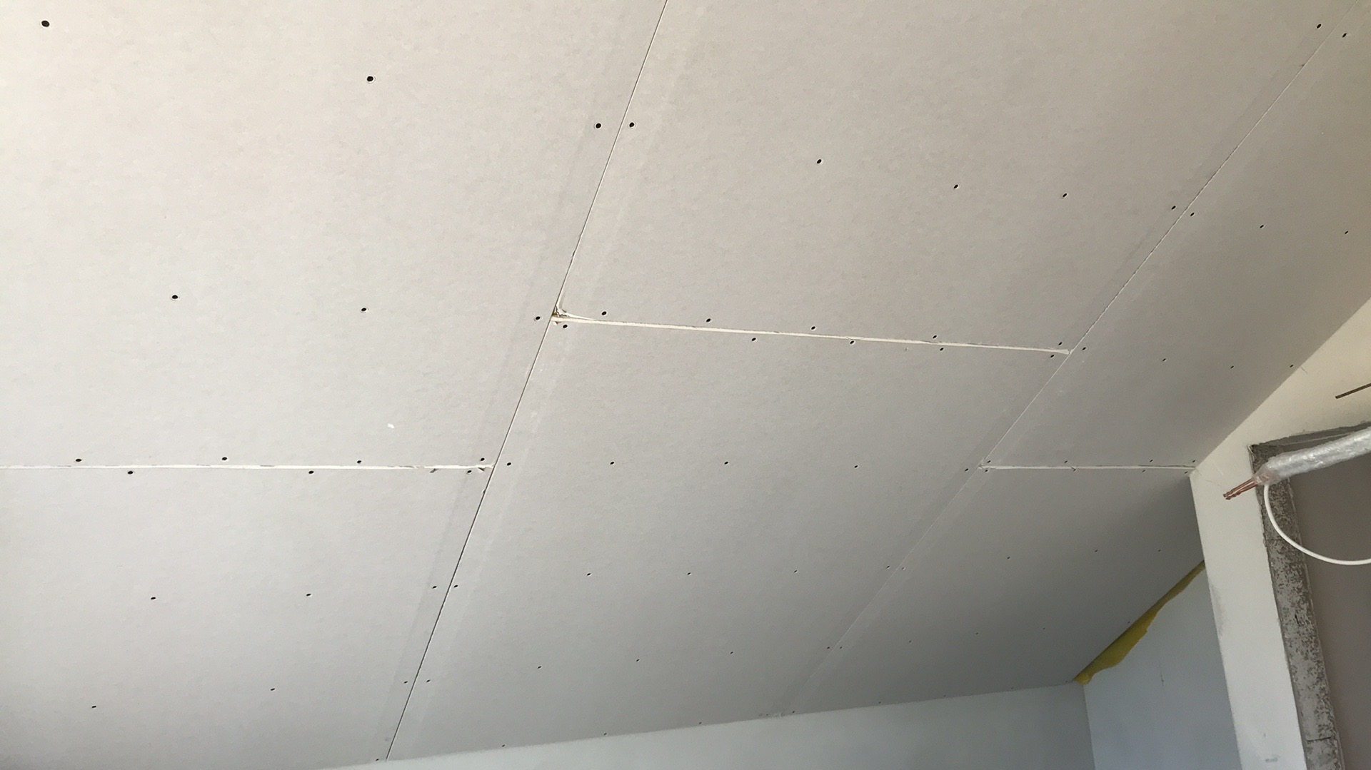 Płyty gipsowo-kartonowe zamontowane na skośnym poddaszu, widoczne ślady po wkrętach, łączenia płyt wypełnione masą szpachlową, fragment ocieplenia widoczny w rogu.