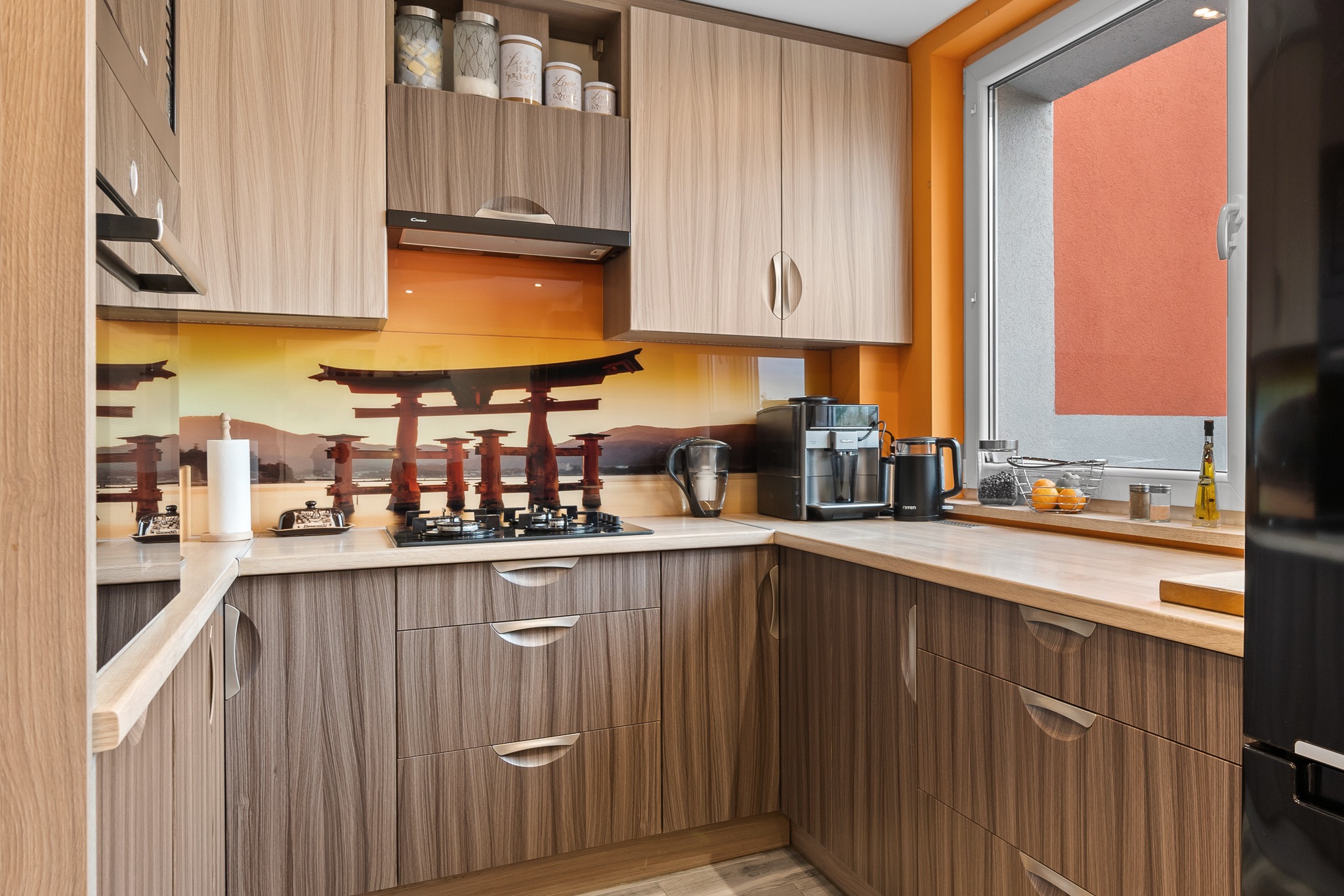 Nowoczesna kuchnia z frontami szafek w dwóch odcieniach drewna, blatem w kolorze jasnego drewna i szklanym panelem nad blatem z motywem japońskiej architektury