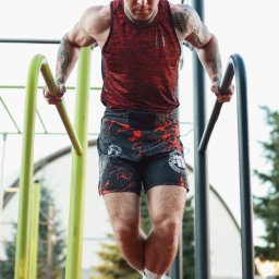 Szymon Citak - Mężczyzna z tatuażami na rękach wykonuje ćwiczenie na poręczach na zewnątrz, ubrany w sportowy strój.