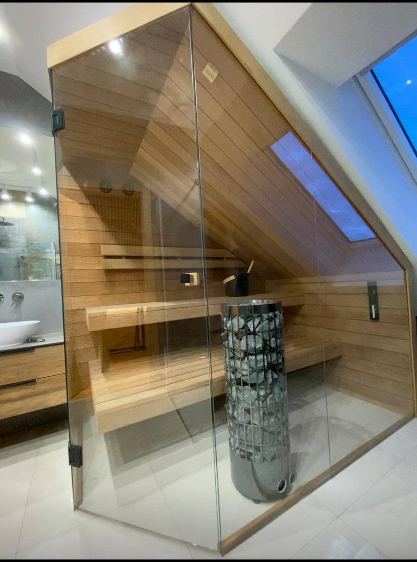 Nowoczesna sauna z osiki termo z dużą ilością przeszkleń, widoczny piec na kamienie, drewniane ławki i okno dachowe.