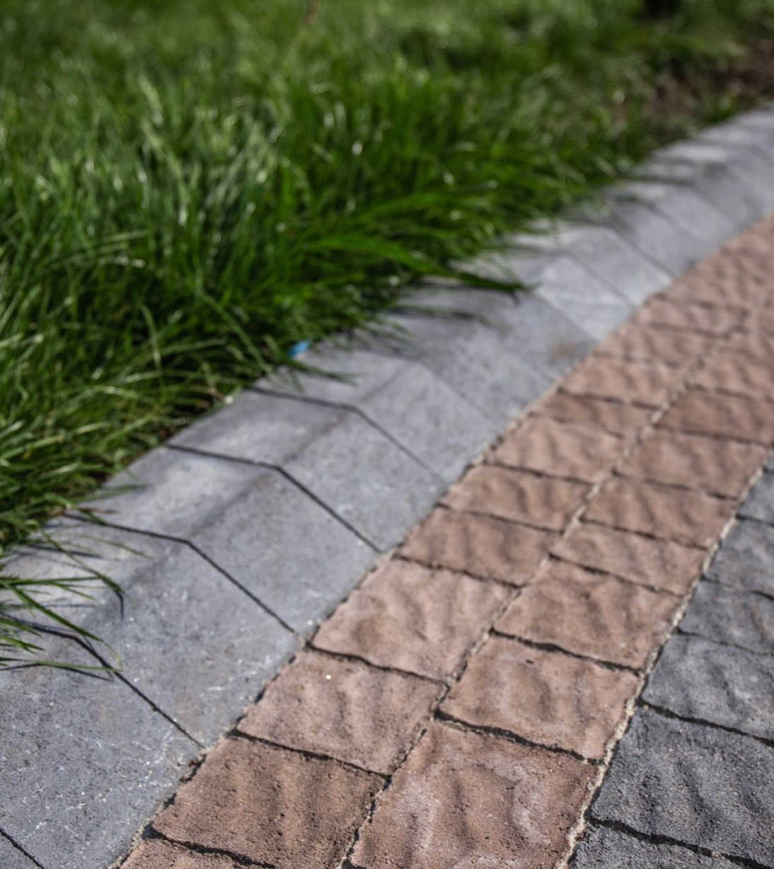 Ścieżka z kostki brukowej w odcieniach szarości i brązu, obrzeże z szarej kostki, przylegająca do trawnika, wykonana z dbałością o szczegóły.
