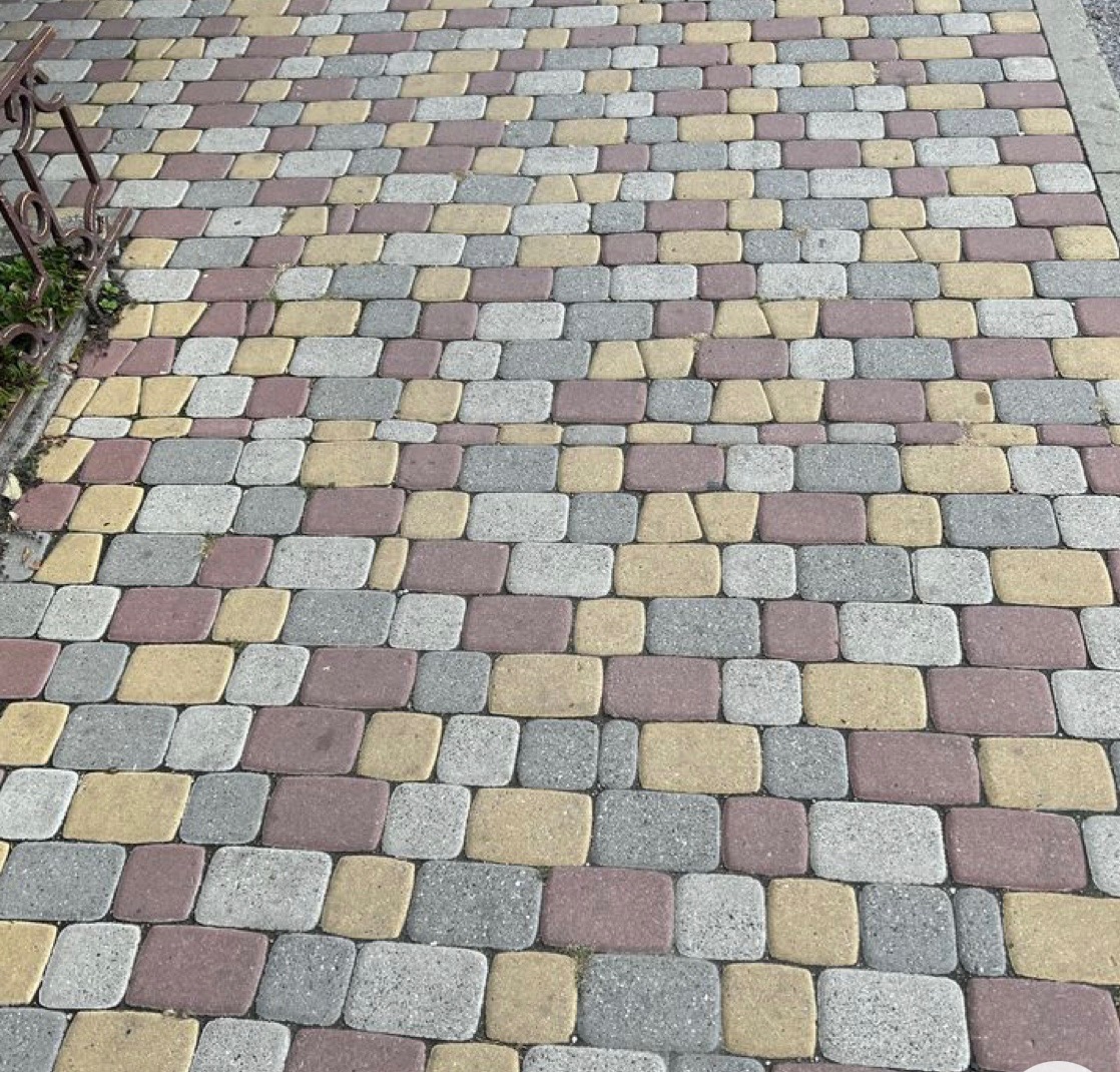 Ułożona kostka brukowa w odcieniach szarości, czerwieni i żółci, widok z góry, z fragmentem metalowego ogrodzenia po lewej stronie.