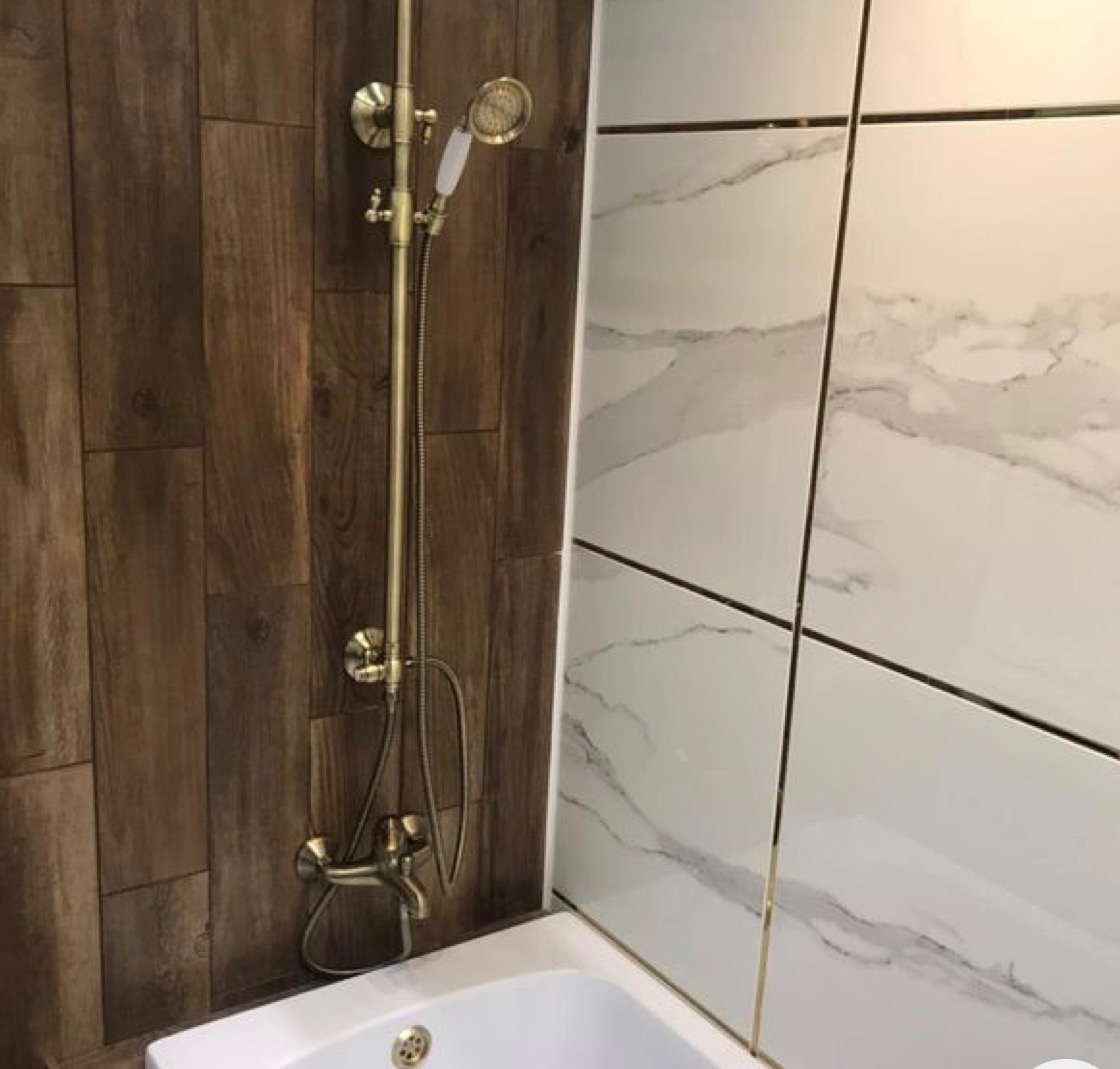 Łazienka z brązowymi panelami ściennymi imitującymi drewno, białą wanną i armaturą w kolorze starego złota, w tym bateria wannowa z deszczownicą i słuchawką.