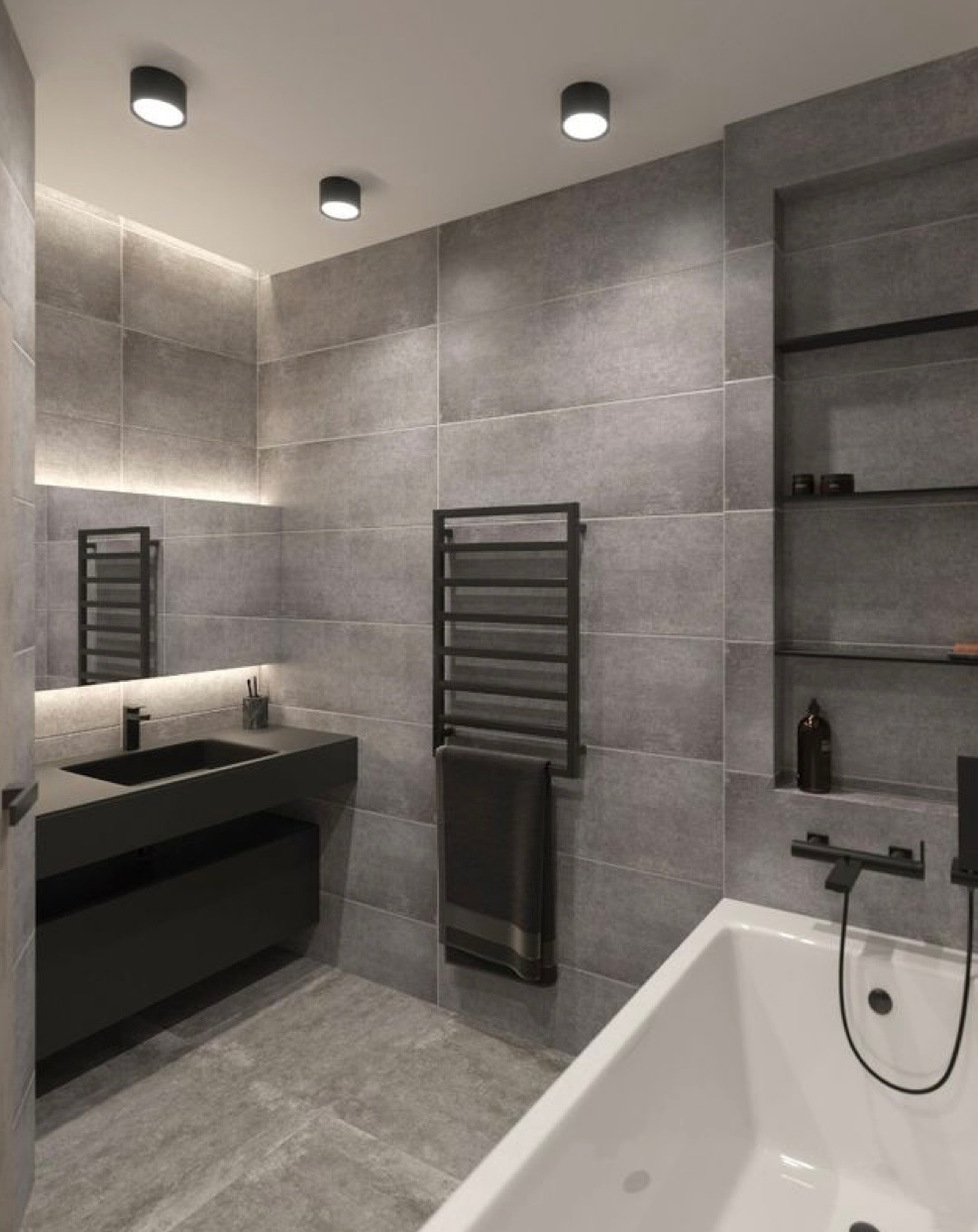 Nowoczesna łazienka w odcieniach szarości z czarnymi akcentami: umywalka nablatowa, grzejnik drabinkowy z powieszonym ręcznikiem, wanna oraz półki wnękowe z dekoracjami.