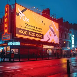 AGENCJA REKLAMY FUX SP.Z O.O. - Duży billboard reklamowy z żółtym tłem i czarnymi elementami graficznymi, umieszczony w miejskiej scenerii nocą, oświetlony neonami i lampami ulicznymi, odbijający się w mokrej nawierzchni ulicy.