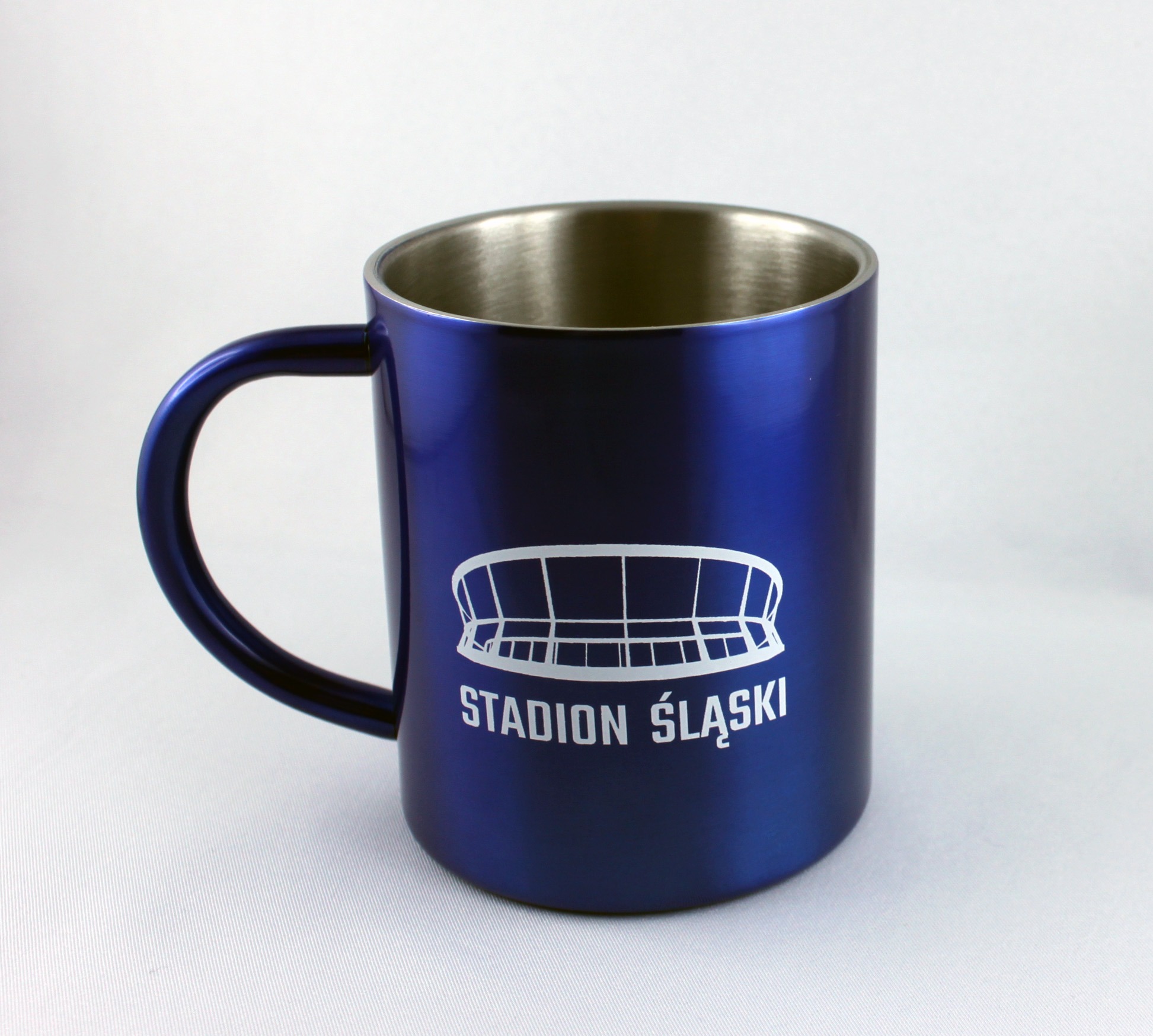 Błyszczący, metaliczny, granatowy kubek z białym nadrukiem Stadionu Śląskiego, na jasnym tle.