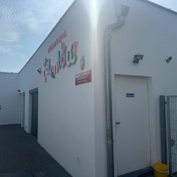 “ J&P.B ” Mycie dachów i elewacji - Biały budynek przedszkola z kolorowym napisem 'Akademia Talentów', widoczne rynny, lampy zewnętrzne i kostka brukowa przed budynkiem.