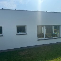 “ J&P.B ” Mycie dachów i elewacji - Boczny widok białej elewacji domu jednorodzinnego z trzema oknami, widoczne rynna i trawnik przed budynkiem w słoneczny dzień.
