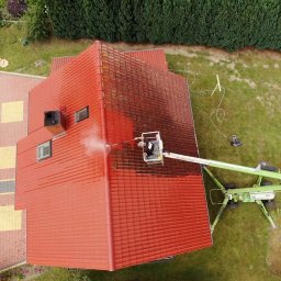 “ J&P.B ” Mycie dachów i elewacji - Widok z góry na czerwony dach z dachówki podczas czyszczenia myjką ciśnieniową z podnośnika koszowego; część dachu umyta, druga pokryta mchem i zabrudzeniami.