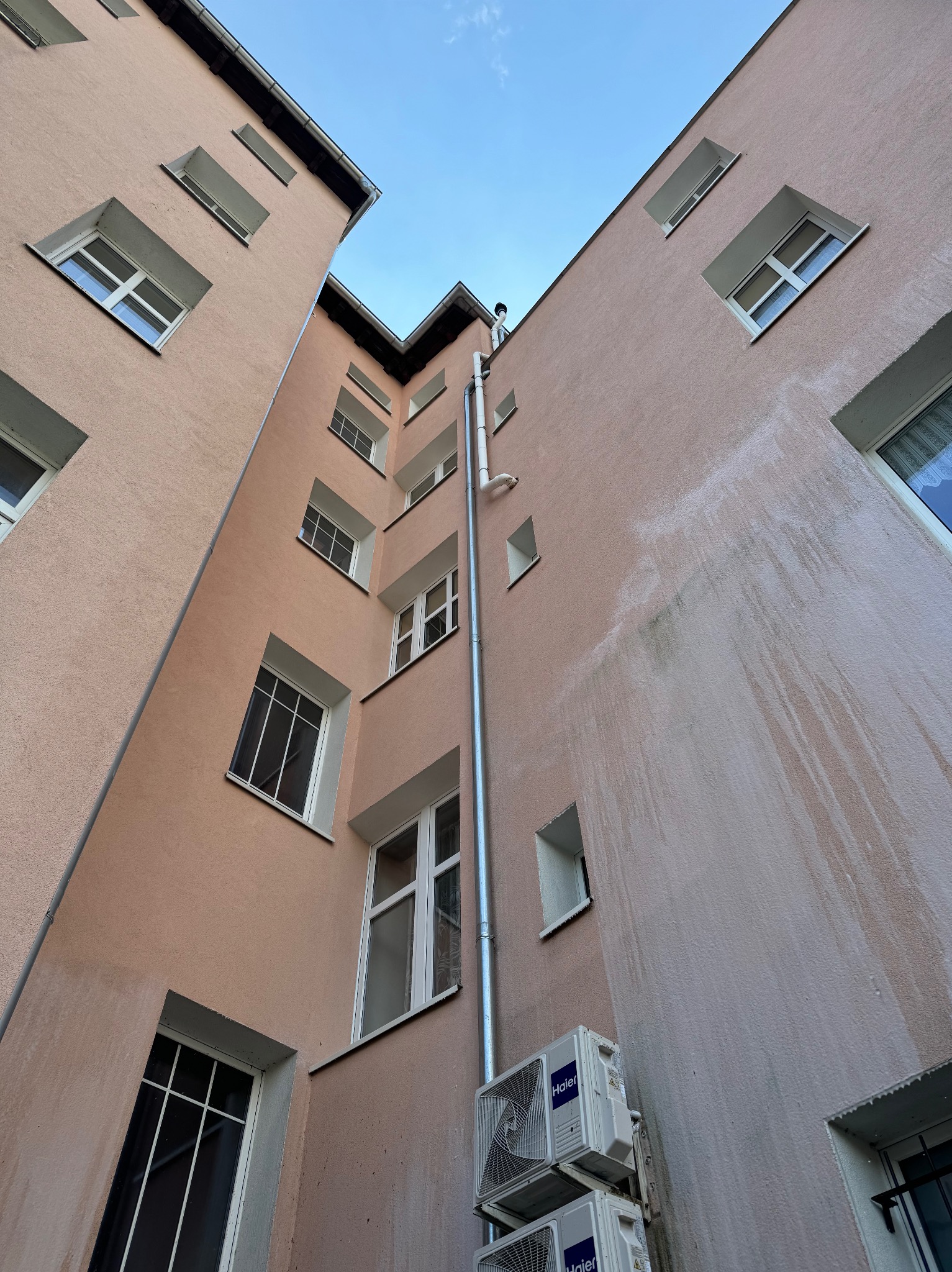 Widok z dołu na elewację budynku z widocznymi śladami po niedokładnym czyszczeniu, rynną i dwoma klimatyzatorami Haier.