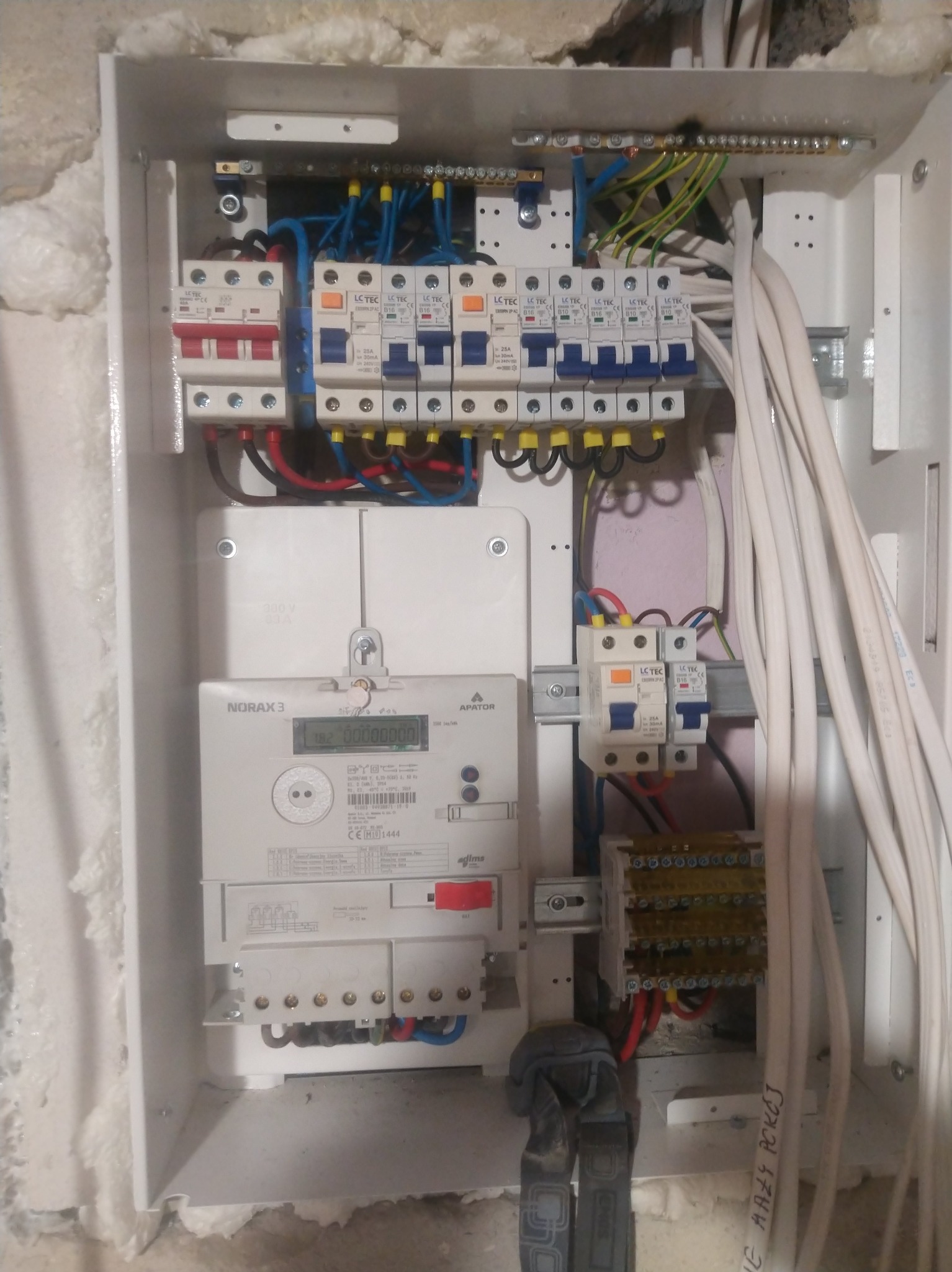 Rozdzielnia elektryczna w trakcie montażu, widoczne bezpieczniki, przewody, licznik energii, osprzęt instalacyjny i narzędzia.