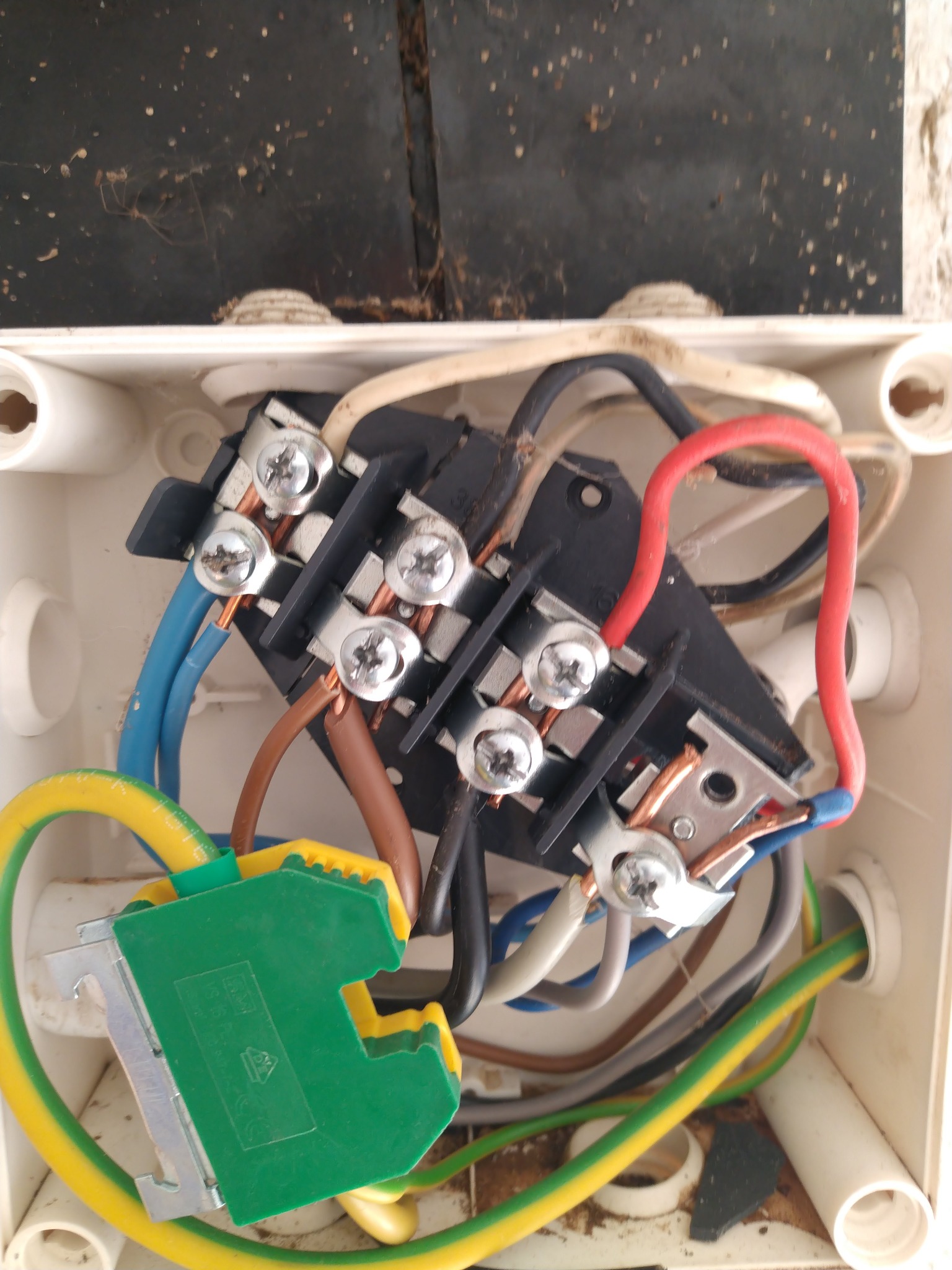 Wnętrze białej puszki elektrycznej z podłączonymi przewodami o różnych kolorach, widoczne śruby mocujące i elementy z tworzywa sztucznego. Ujęcie z bliska, z góry.