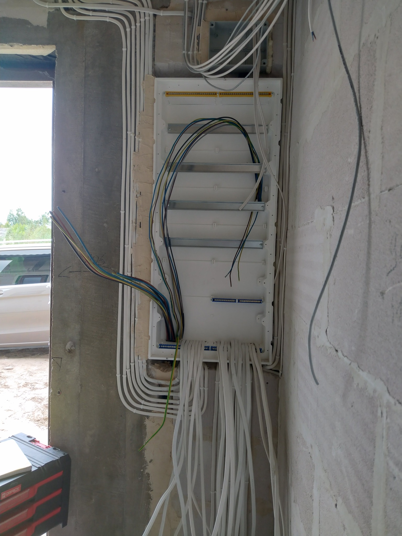 Rozdzielnia elektryczna w surowym wnętrzu. Białe kable prowadzone w peszlach, widoczne przewody zasilające. Montaż w trakcie prac wykończeniowych.