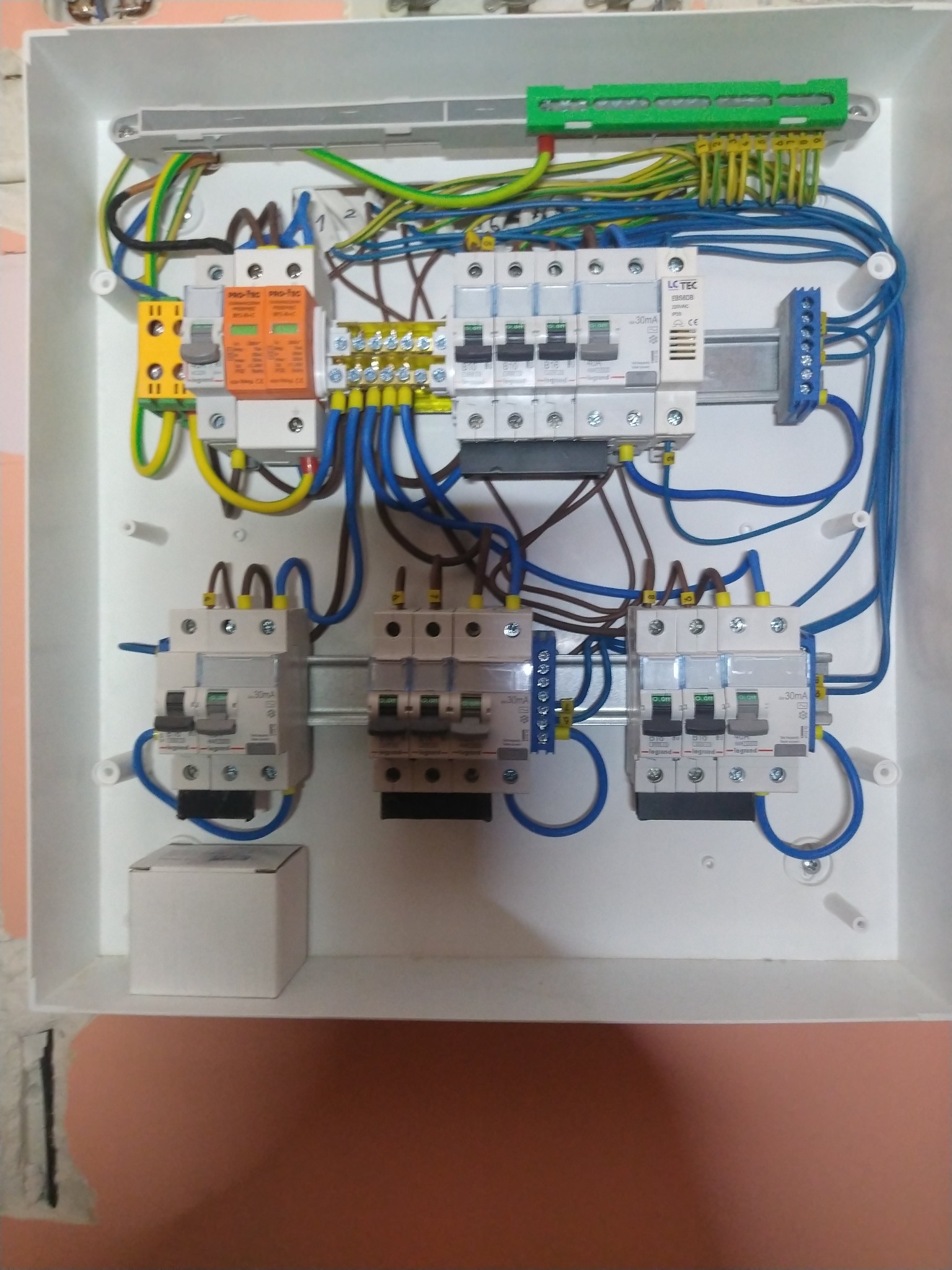 Rozdzielnica elektryczna w białej obudowie z widocznymi bezpiecznikami, przewodami w różnych kolorach i elementami montażowymi. Widok z góry na zamontowaną instalację.