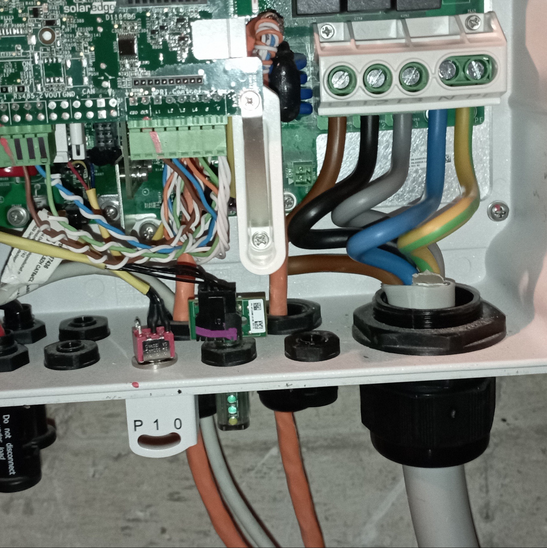 Wnętrze skrzynki elektrycznej z widocznymi przewodami, złączkami i płytką drukowaną. Elementy instalacji fotowoltaicznej SolarEdge z precyzyjnym okablowaniem.