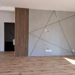 Pokój po remoncie: ściana z szarą gładzią ozdobiona geometrycznym wzorem z czarnych linii, drewniane lamele dekoracyjne, panele podłogowe imitujące drewno.