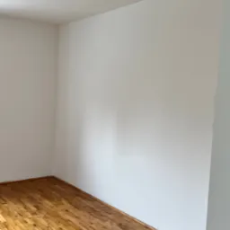 Pusty pokój z parkietem w jodełkę i świeżo pomalowanymi na biało ścianami, widok z narożnika, jasne światło dzienne.