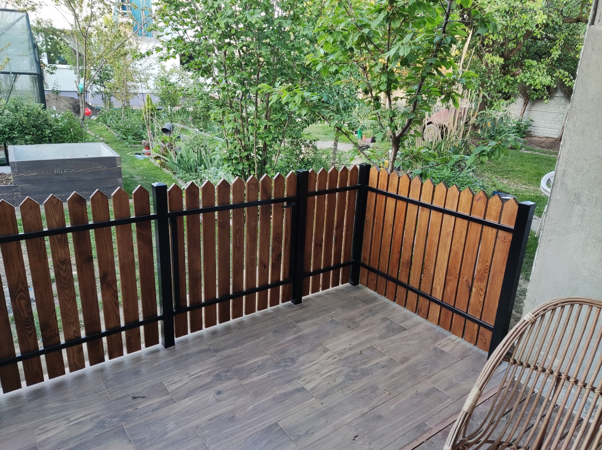 Drewniany płot z czarną metalową ramą na tarasie z widokiem na zielony ogród.