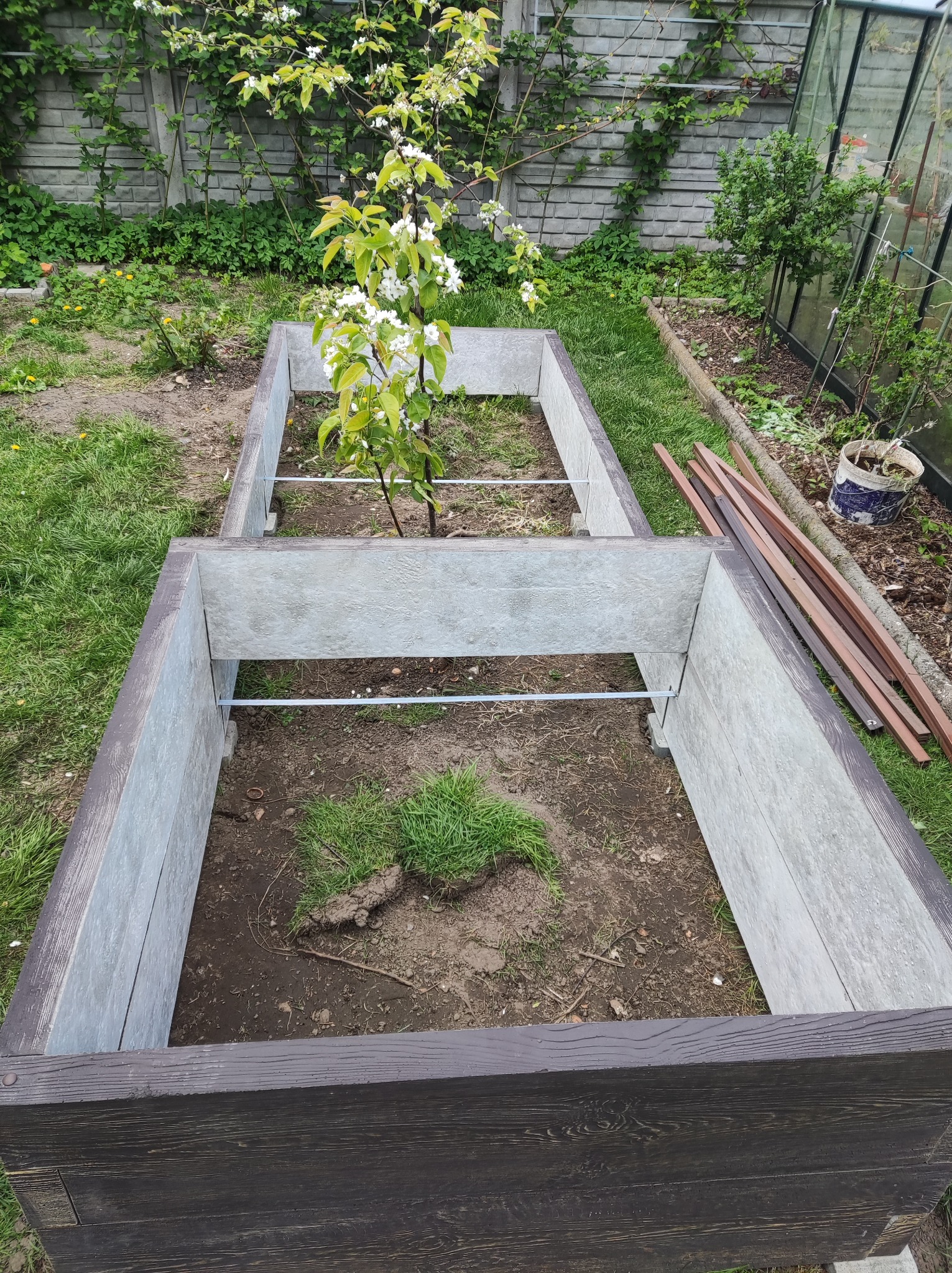 Nowa, podwyższona rabata z desek kompozytowych w Ulanowie, z młodym drzewkiem owocowym w centralnej części i widocznymi elementami konstrukcyjnymi.