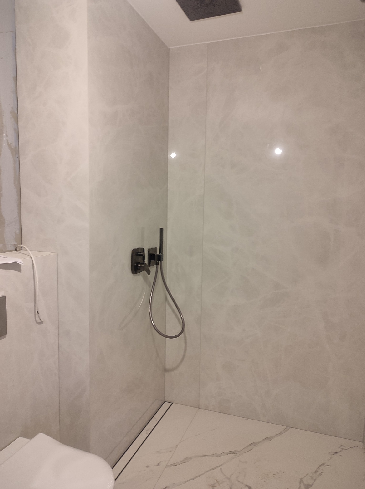 Nowoczesna kabina prysznicowa walk-in z szarymi marmurowymi płytkami na ścianach i podłodze, czarna bateria podtynkowa, odpływ liniowy.