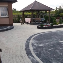 EKOPLANET Sp. z o.o. - Ułożona kostka brukowa w dwóch odcieniach szarości tworząca wzór na podjeździe z altaną w ogrodzie, widoczny rower oparty o filar altany.