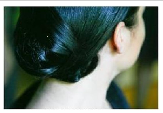 Elegancka fryzura upięta z tyłu głowy, ciemne, gładkie włosy splecione w kok na karku, widoczny fragment ucha i szyi modelki.