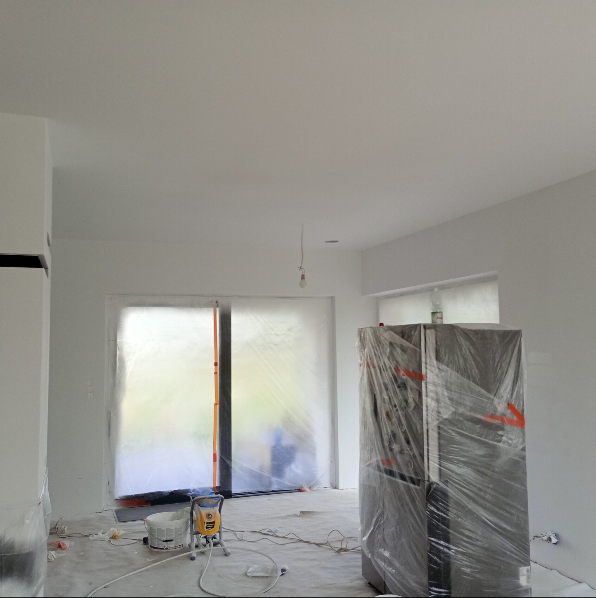 Przygotowanie do malowania: pomieszczenie zabezpieczone folią, sprzęt malarski i wiadro z farbą na podłodze, meble okryte folią ochronną.