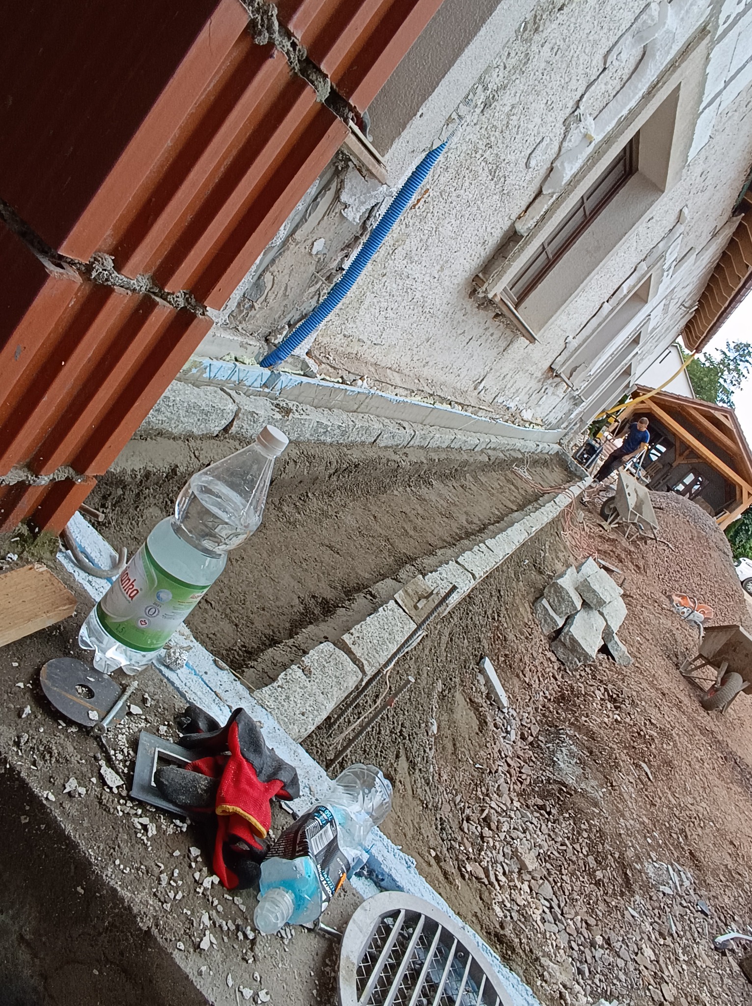 Przygotowanie terenu pod obrzeże z kostki granitowej, widoczny wykop, ułożone obrzeże, narzędzia i butelka wody na pierwszym planie, pracownik w oddali.