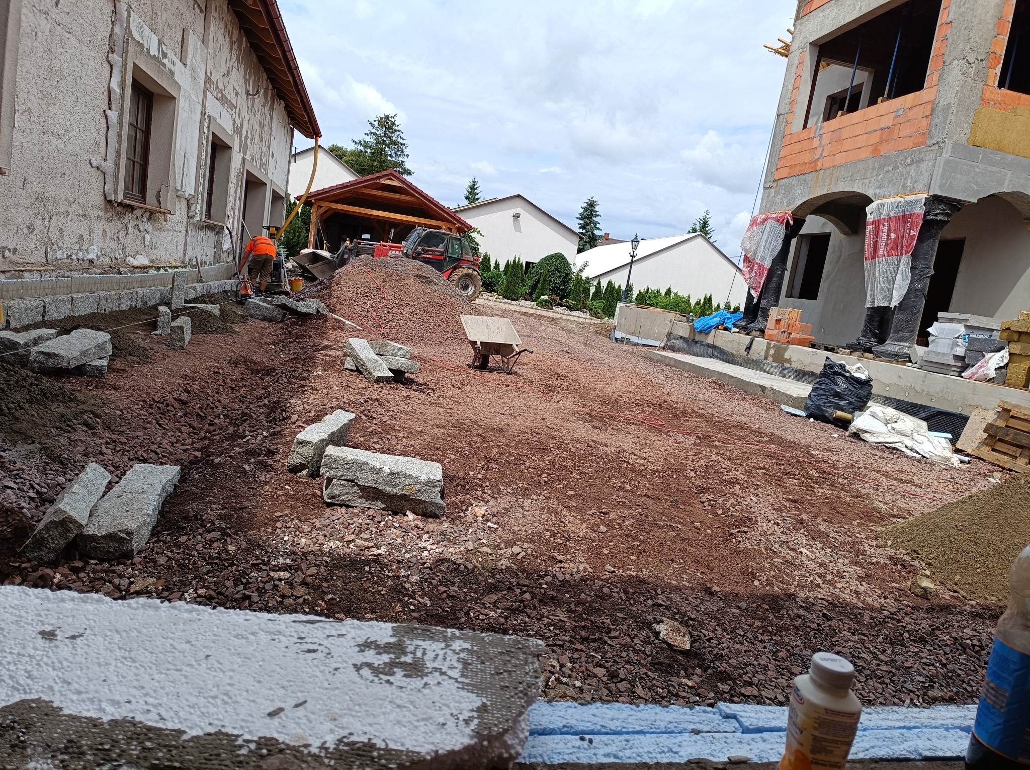 Prace przygotowawcze do ułożenia nawierzchni w Świdnicy: wyrównywanie terenu podłoża z gruzem i kamieniami, widoczny pracownik z pomarańczową kamizelką, przygotowane bloki granitowe i budynek...