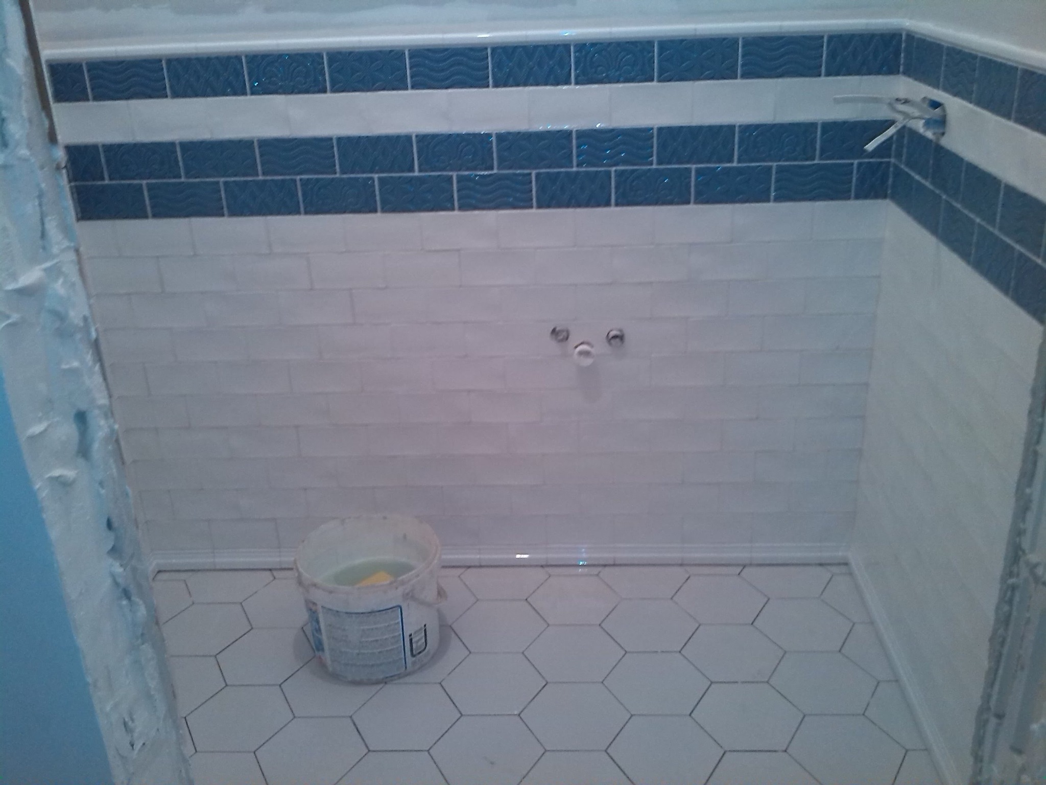 Wykończona łazienka z białymi heksagonalnymi płytkami podłogowymi i białymi cegiełkami na ścianach, akcentowana niebieskimi dekoracyjnymi pasami płytek.