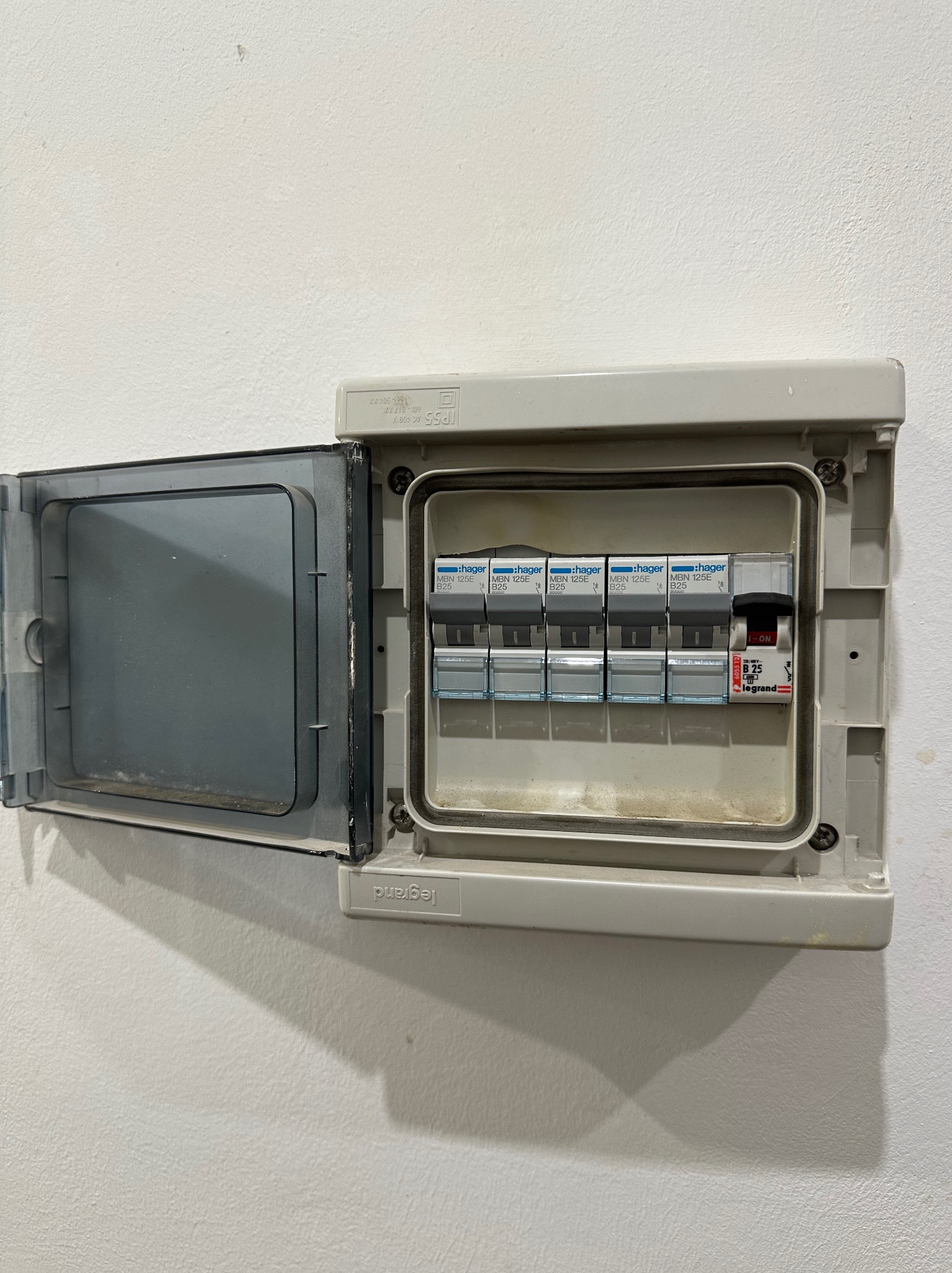 Otwarta skrzynka bezpiecznikowa marki Legrand i Hager, zamontowana na białej ścianie, widoczne bezpieczniki typu B25.