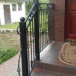 Zakład Usług Leśnych Robert Kowalski,Usługi budowlane - Czarne, metalowe schody zewnętrzne z ozdobnymi elementami, prowadzące do drzwi wejściowych z brązowej cegły.