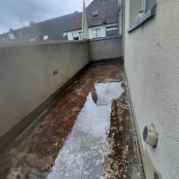 Zakład Usług Leśnych Robert Kowalski,Usługi budowlane - Zalany, brudny balkon z widocznymi śladami starej farby i wody, z szarymi ścianami i fragmentem budynku w tle.