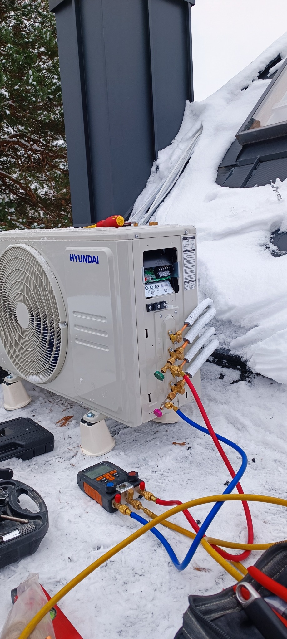 Zewnętrzna jednostka klimatyzacji Hyundai zamontowana na dachu pokrytym śniegiem, widoczne podłączenia rur chłodniczych i narzędzia pomiarowe, trwają prace instalacyjne.