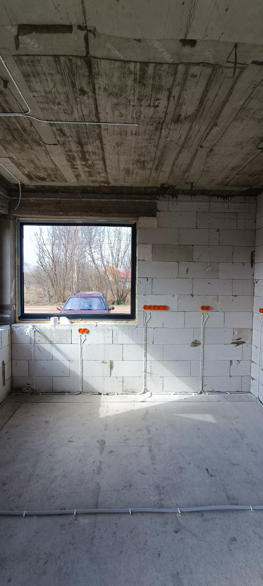 Surowy stan wnętrza budynku w Białymstoku z widocznymi instalacjami elektrycznymi w ścianach z betonu komórkowego i rurami wentylacyjnymi na podłodze, okno z widokiem na zewnątrz.