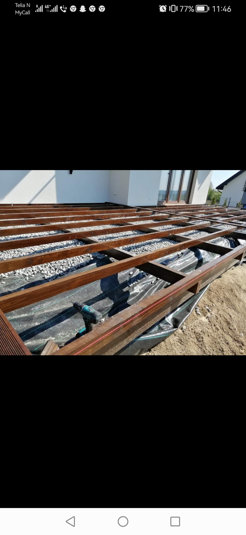 Konstrukcja nośna tarasu z belek drewnianych, podsypana białym grysem, z widoczną wkrętarką akumulatorową na czarnej geowłókninie.