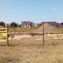 EXIGOBUD RAFAŁ STEFAŃSKI - Fundamenty domu jednorodzinnego w trakcie budowy, widoczna żółta tablica informacyjna z napisem 'Kierownik Budowy', w tle zabudowa jednorodzinna i wielorodzinna.