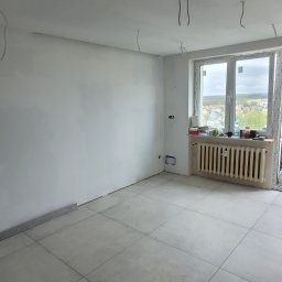 Cts fiszka - Wyremontowane wnętrze w Rumi z szarą podłogą z płytek, przygotowane do dalszych prac wykończeniowych, z widocznymi przewodami elektrycznymi zwisającymi z sufitu.