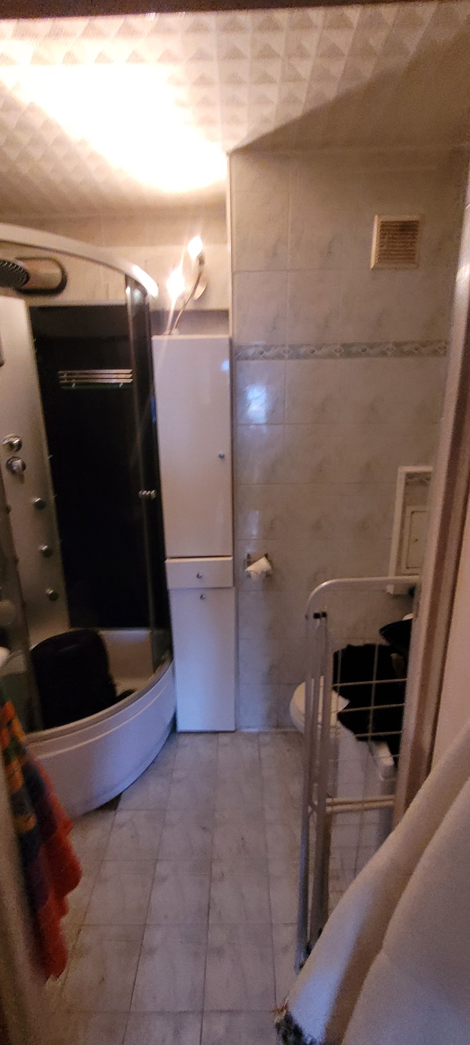 Wnętrze łazienki po remoncie: kabina prysznicowa z hydromasażem, biała szafka łazienkowa, płytki ceramiczne na ścianach i podłodze, grzejnik drabinkowy, oświetlenie sufitowe.