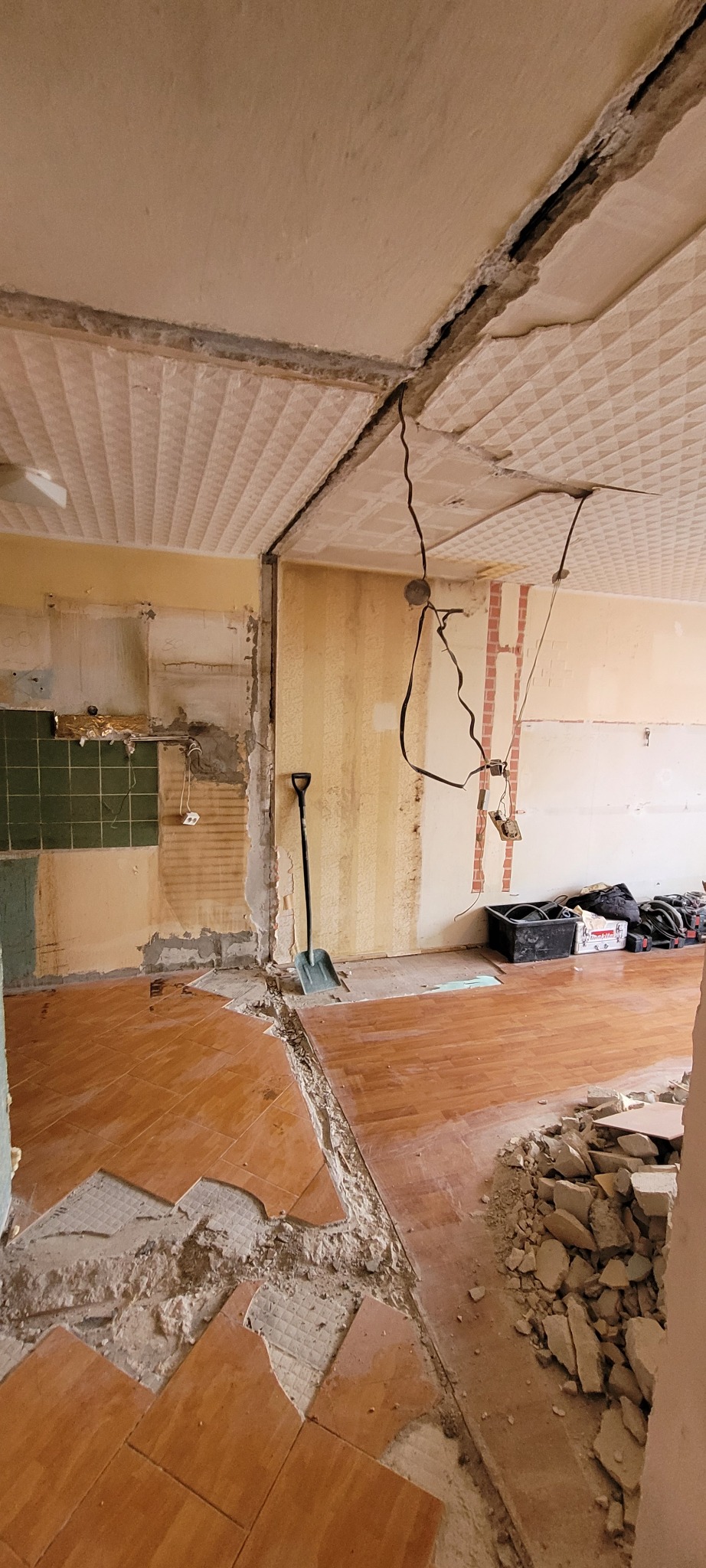 Demontaż starej podłogi z płytek w trakcie remontu kuchni, widoczne odsłonięte kable elektryczne i fragmenty starej instalacji pod sufitem.