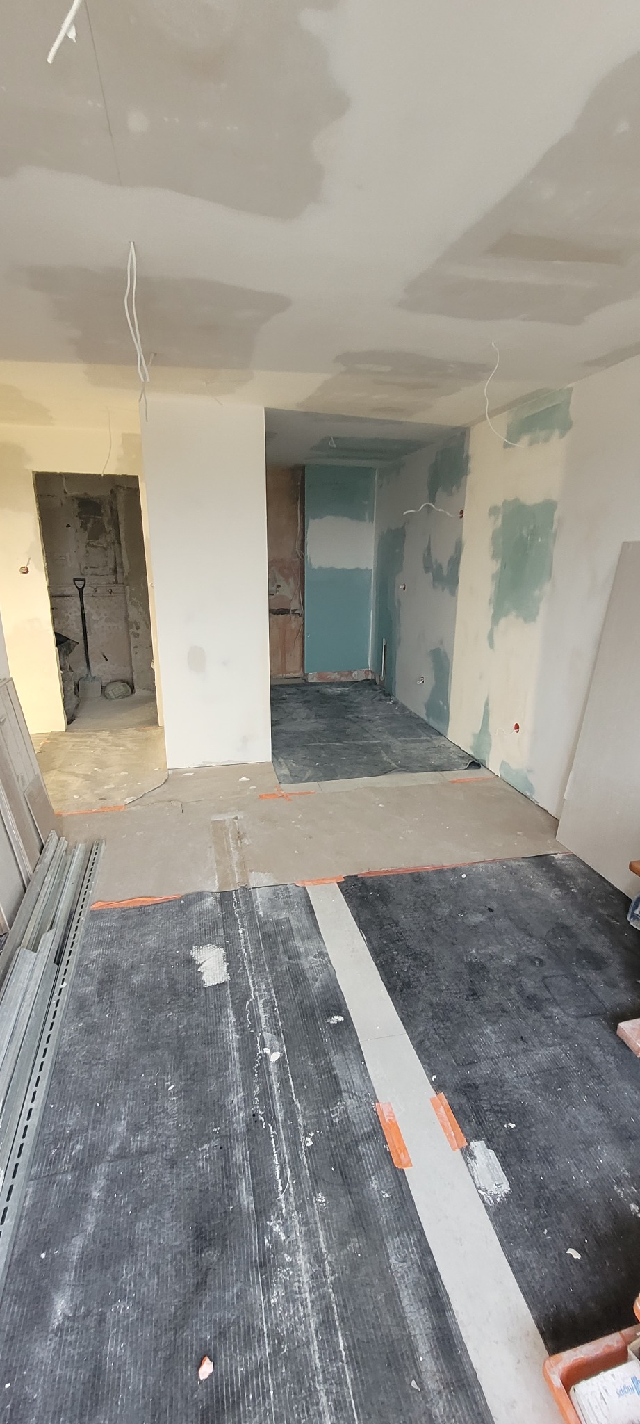 Wnętrze w trakcie remontu: częściowo położona gładź na ścianach, odsłonięte kable sufitowe, zabezpieczona podłoga i profile do płyt gipsowo-kartonowych.