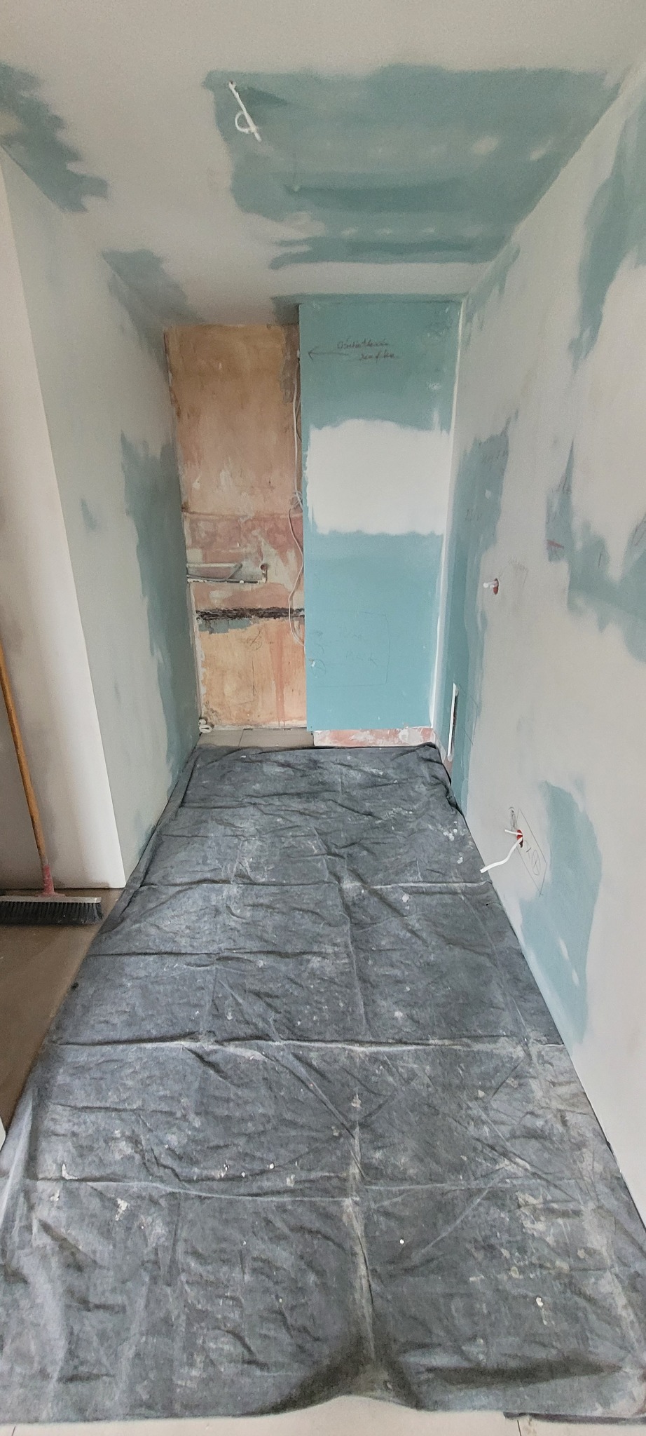 Pokój w trakcie remontu: ściany częściowo pokryte gładzią, podłoga zabezpieczona folią malarską, widoczne kable elektryczne wystające ze ściany.