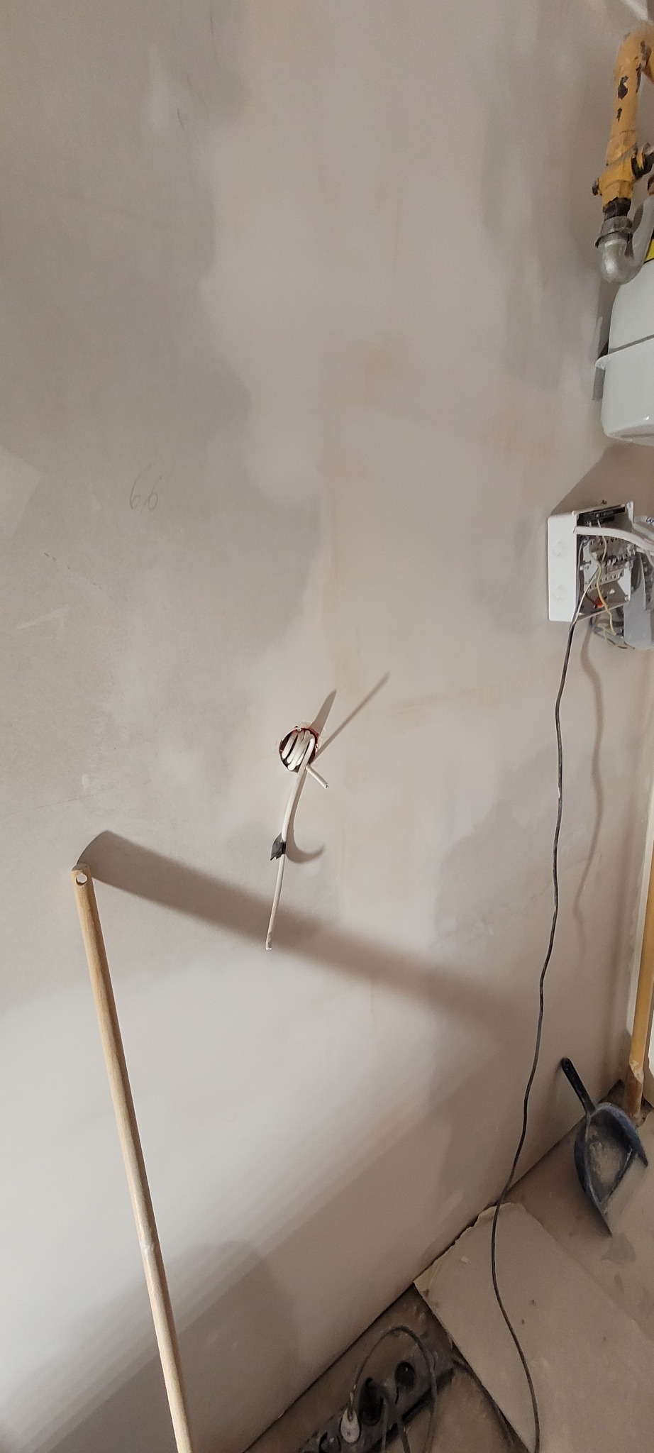 Ściana po nałożeniu gładzi, widoczne wystające przewody elektryczne, rurka oraz narzędzia do sprzątania.
