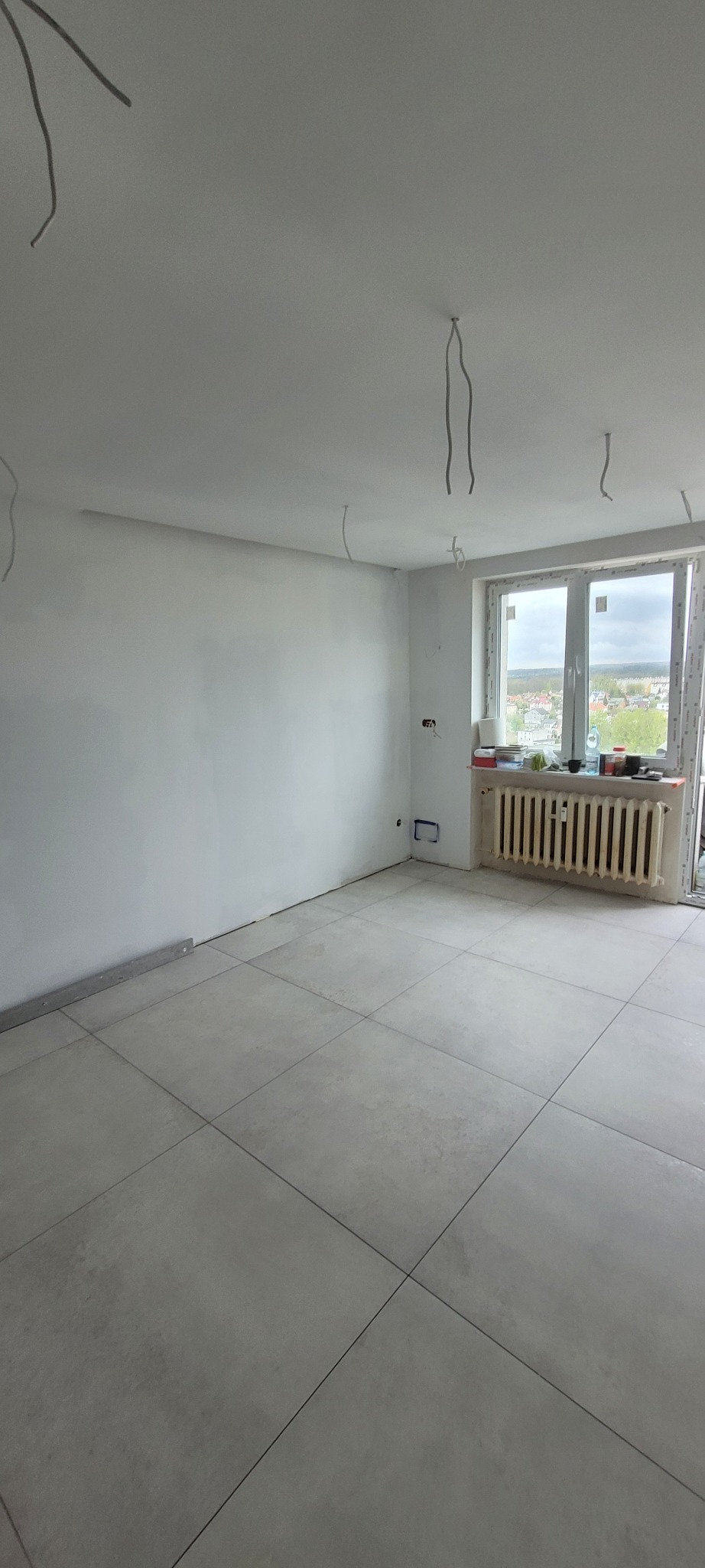 Wyremontowane wnętrze w Rumi z szarą podłogą z płytek, przygotowane do dalszych prac wykończeniowych, z widocznymi przewodami elektrycznymi zwisającymi z sufitu.