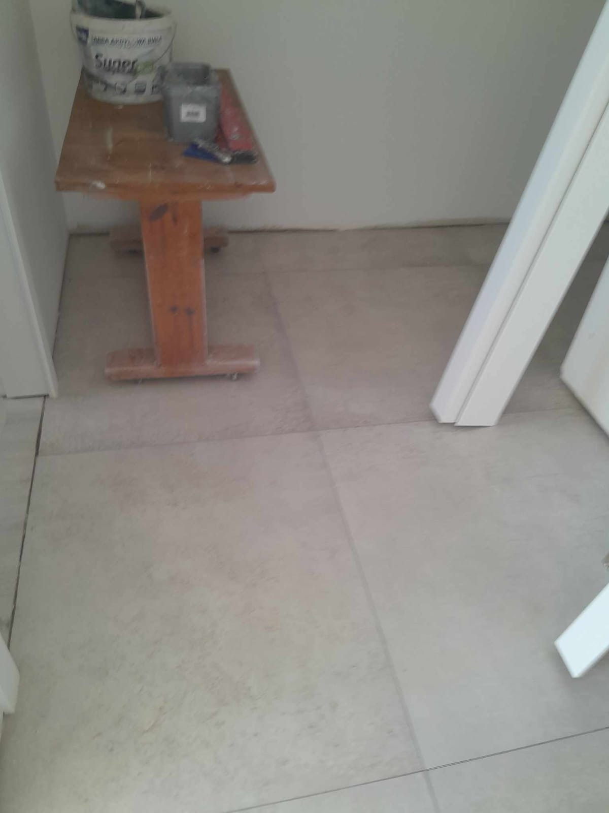 Ułożone jasnoszare płytki podłogowe z widocznym stolikiem z narzędziami i wiadrem farby w rogu pomieszczenia.