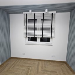 Michael Berg - Pokój po remoncie: drewniana podłoga ułożona w jodełkę, białe ściany z szarymi panelami dekoracyjnymi na ścianach i suficie, okno z białymi żaluzjami z czarnymi taśmami.