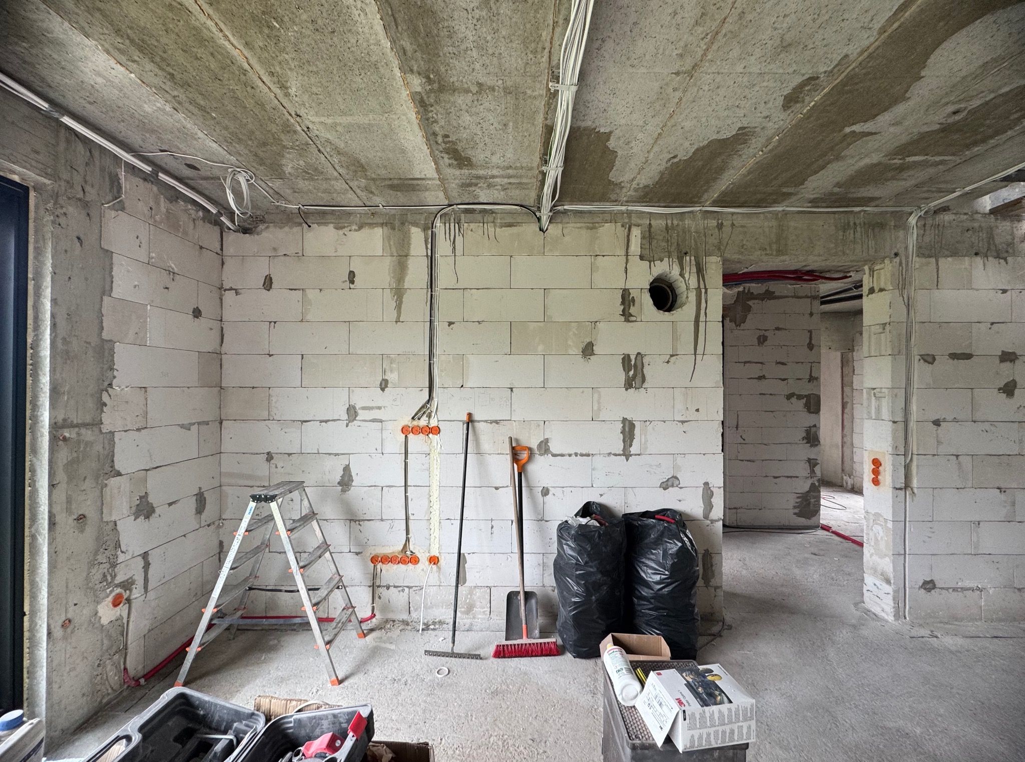 Wnętrze w trakcie prac wykończeniowych: widoczne przewody elektryczne przy suficie, puszki instalacyjne w ścianach z betonu komórkowego oraz drabina i narzędzia.