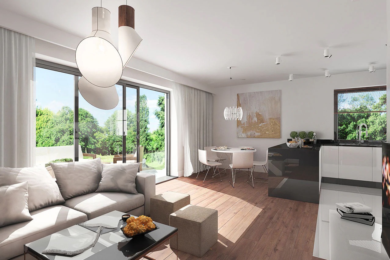 Jasne, przestronne wnętrze salonu z dużym oknem balkonowym i widokiem na zieleń, nowoczesna lampa wisząca, drewniana podłoga i minimalistyczna kuchnia w tle.