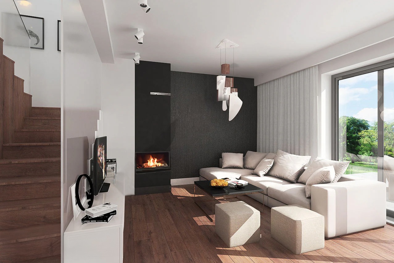 Jasne, przestronne wnętrze salonu z drewnianą podłogą, kominkiem w czarnej obudowie i schodami z drewnianymi stopniami. Duże okno z widokiem na zieleń, nowoczesna lampa wisząca i narożna sofa...